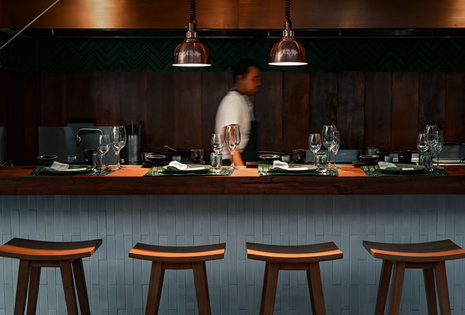 Silhouette of a chef walking behind the counter at the Chef’s Table at Nio, with the beautifully set dining area in the foreground. The ambient lighting and elegant setup highlight the refined atmosphere of this exclusive East-meets-West culinary experience at NIHI Sumba.