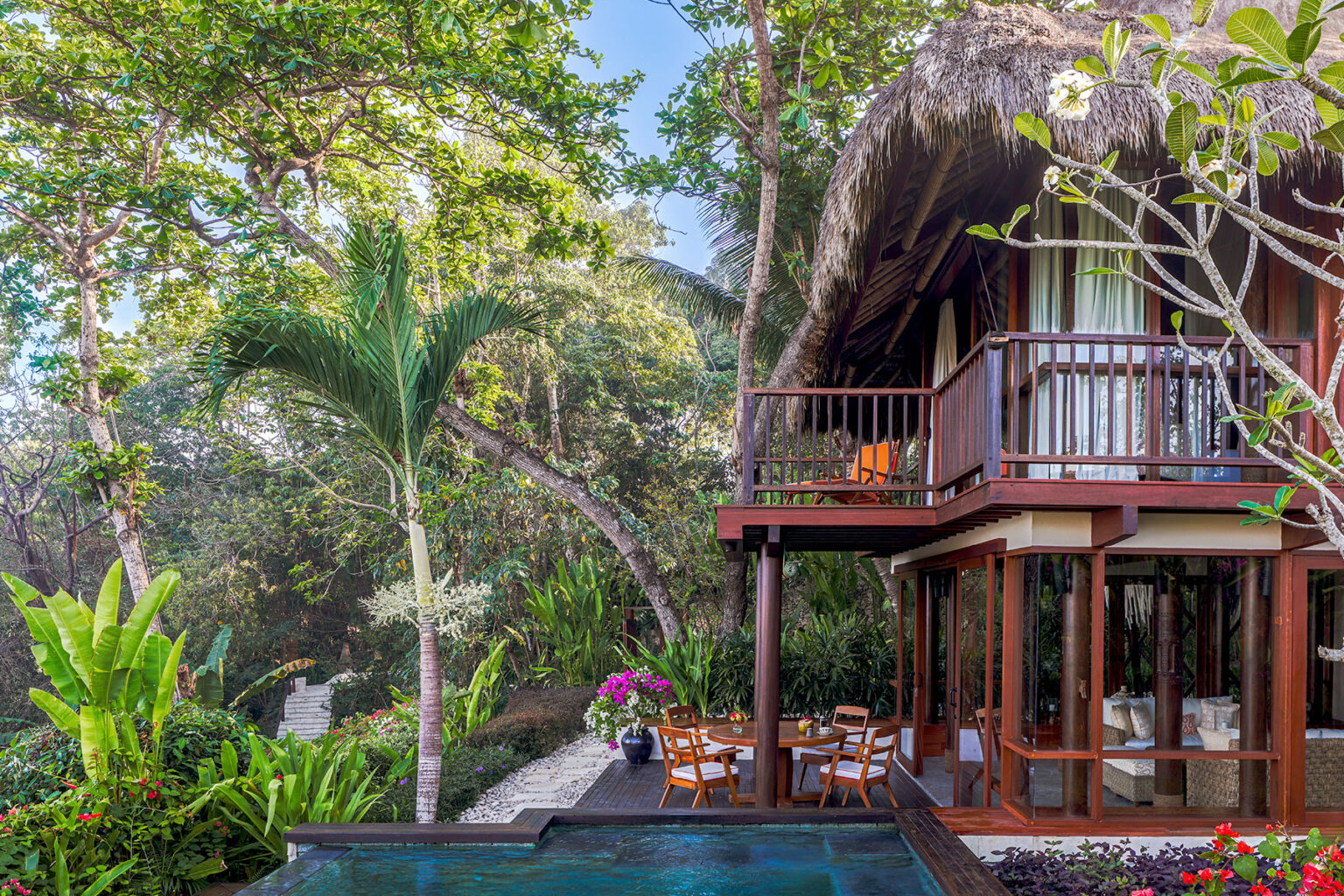 The Kanatar Villa at NIHI® Sumba, showcasing a private dining area next to the plunge pool, with a balcony offering a view of lush greenery and a tropical garden.