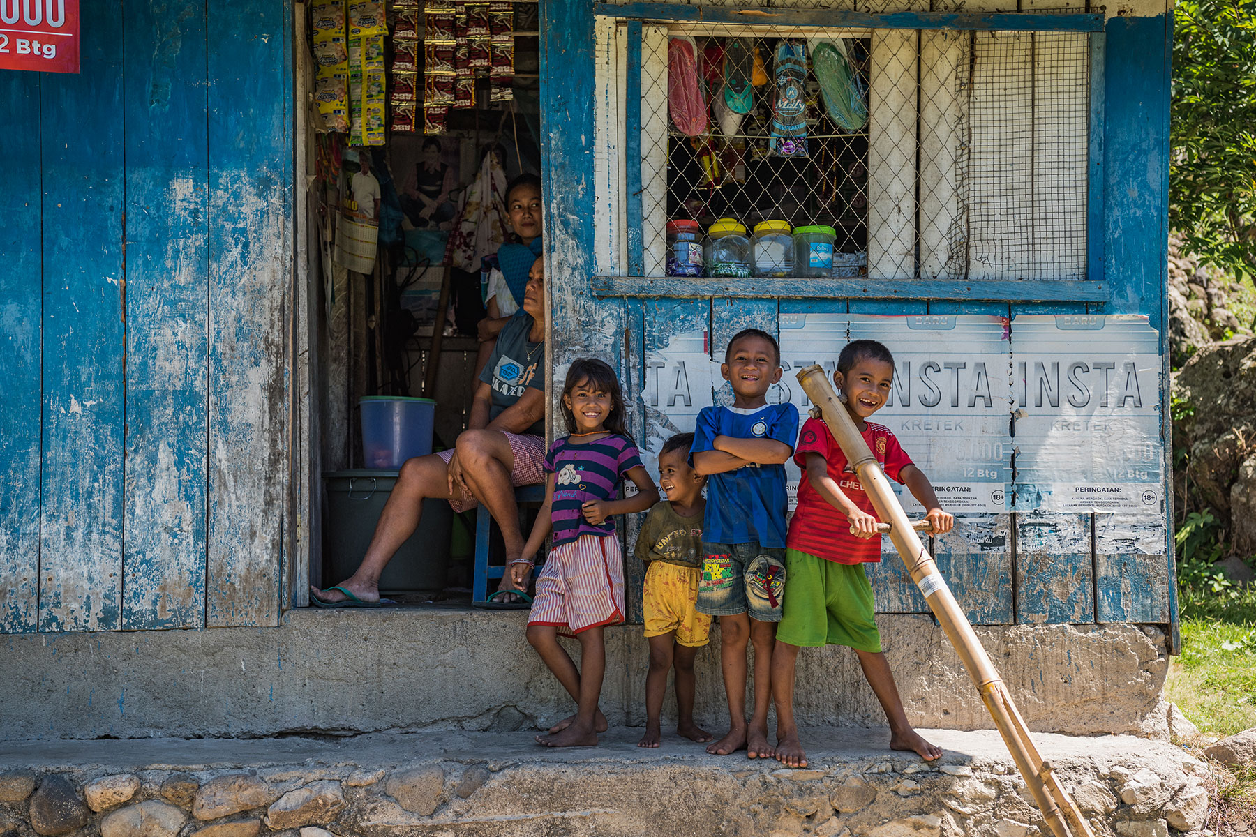 Smiling Sumbanese children standing outside a rustic village shop, showcasing the warmth and charm of local life in rural Sumba.