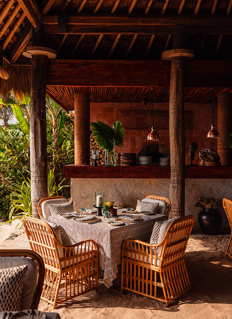 A beautifully set table at Ombak Restaurant, NIHI Sumba, featuring wicker chairs, a linen tablecloth, and tropical decor. The open-air dining space is surrounded by lush greenery, offering a serene and intimate setting for guests to enjoy fresh, locally sourced meals.