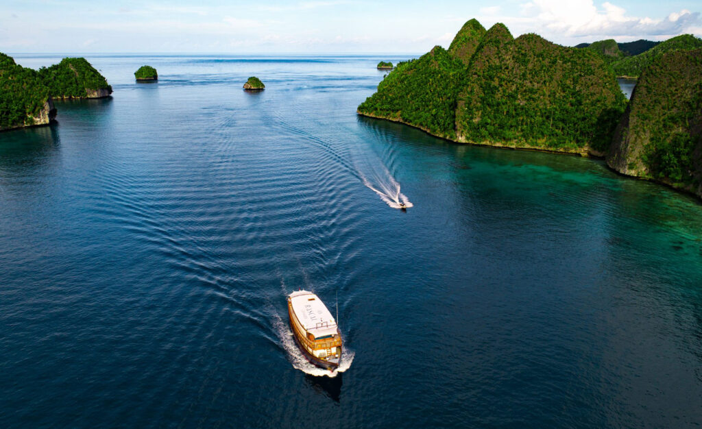 Rascal Voyages luxury yacht cruising through turquoise waters surrounded by lush green tropical islands in Indonesia.