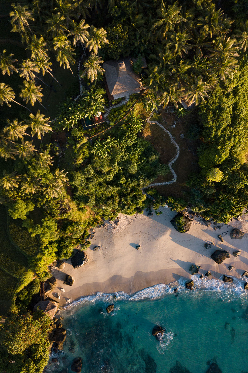 Portrait version of Villa Rahasia stunning aerial view, nestled within lush greenery, overlooking the pristine beach and the vibrant blue waters of the Indian Ocean, offering unparalleled privacy and seclusion.