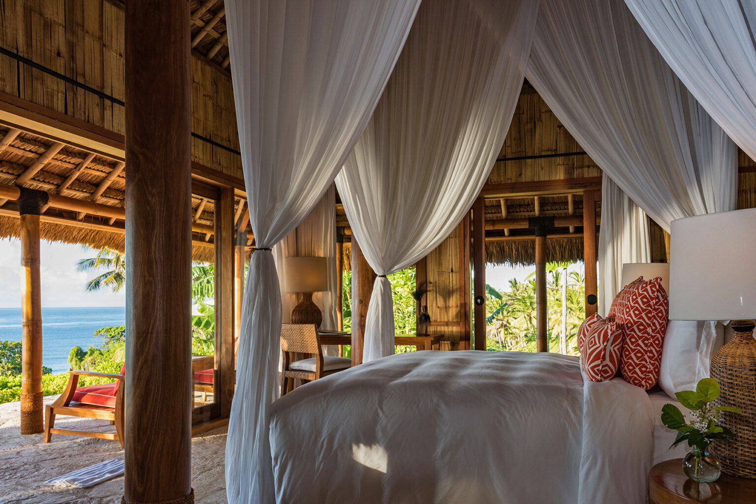 Canopy-draped bed in Villa Rahasia, the only private villa within the grounds of NIHI Sumba’s Nihioka Spa, offering panoramic ocean views, rustic bamboo interiors, and floor-to-ceiling glass doors that blend indoor comfort with surrounding nature. Guests can book it for the first or last night of their stay at the resort.