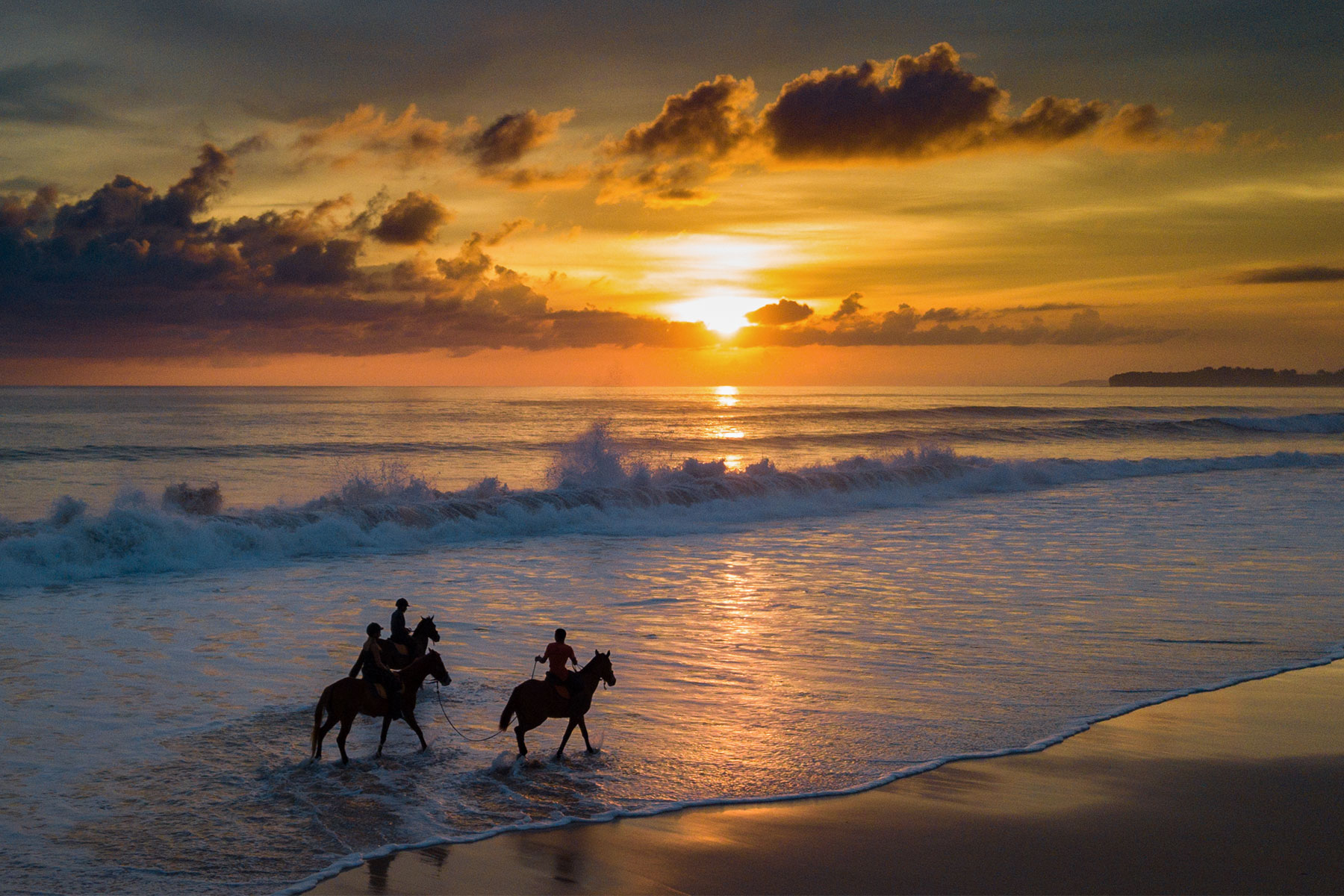 Two riders on Sumba horses are silhouetted against a glowing sunset at Nihiwatu Beach during NIHI Sumba’s Sunset Beach Horse Riding experience.