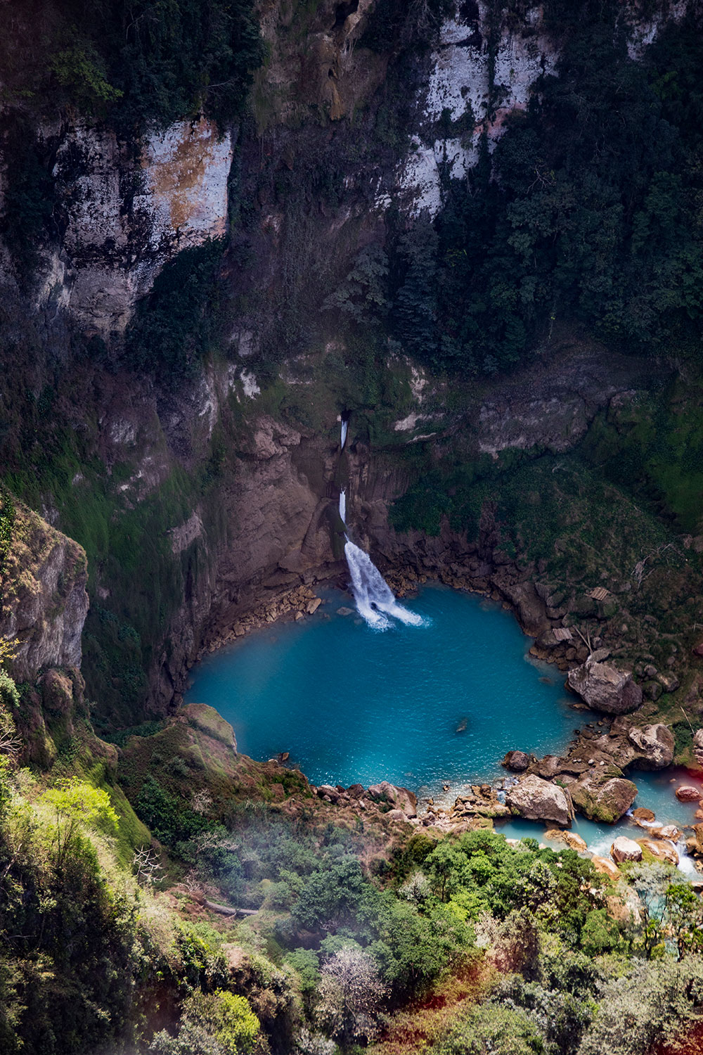 Aerial view of the remote Blue Waterfall, featuring a vivid turquoise plunge pool and natural stone basins surrounded by cliffs and dense jungle.