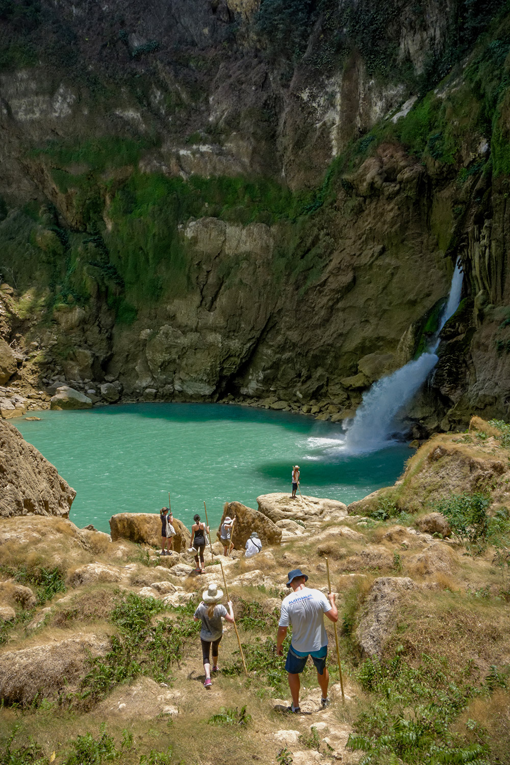 Guests trekking down rocky cliffs toward Blue waterfall in Sumba Island, Indonesia.