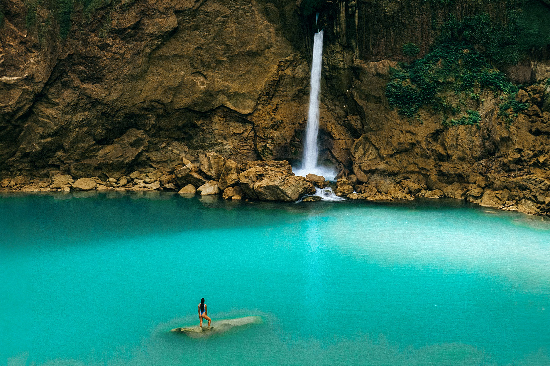 Traveler standing on a rock in turquoise blue lagoon beneath a stunning Matayangu Waterfall in Sumba Island, Indonesia.