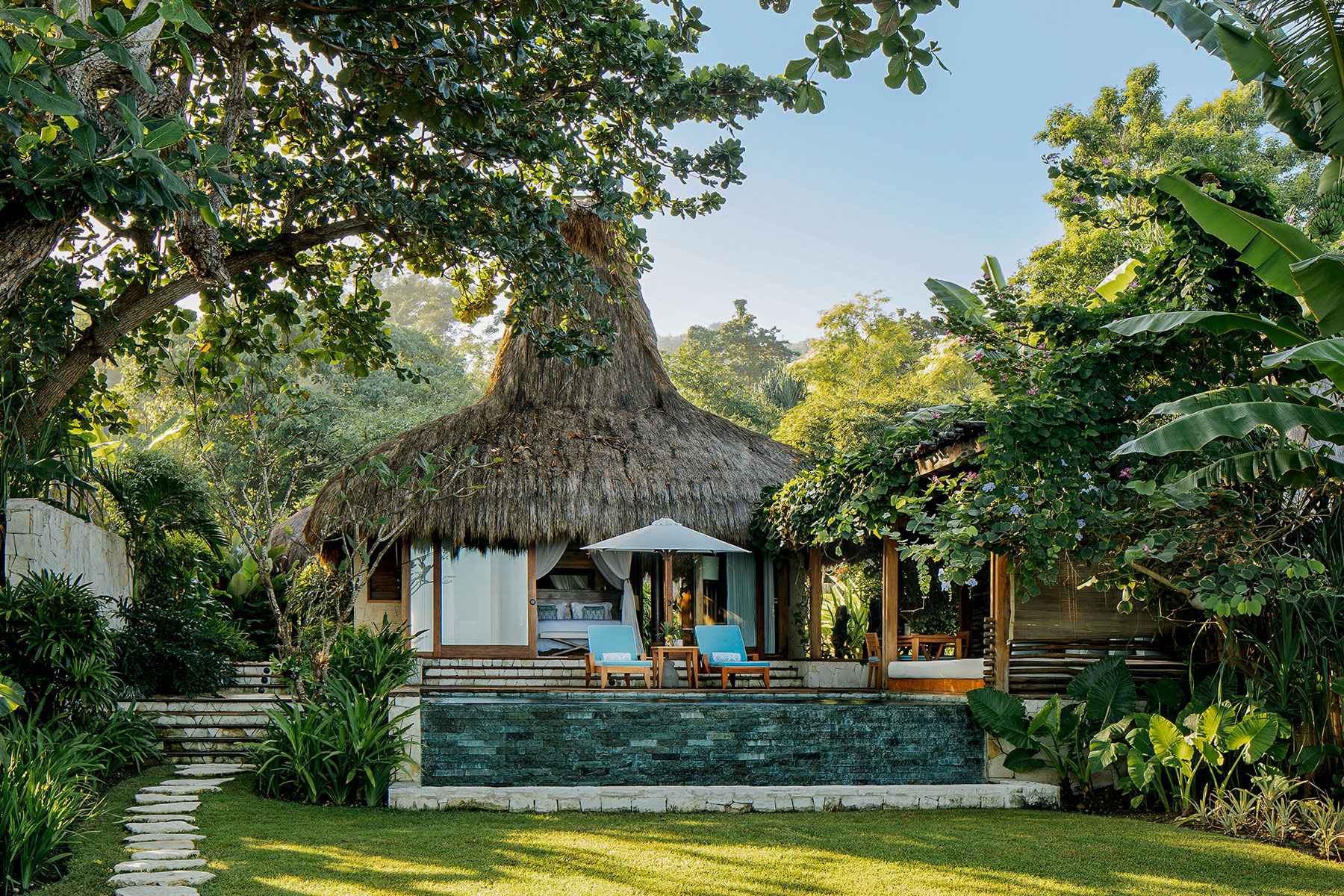 View of the Marangga Villa at NIHI Sumba, featuring a thatched roof, outdoor lounge area, and lush tropical surroundings, showcasing the villa's serene and natural beauty.