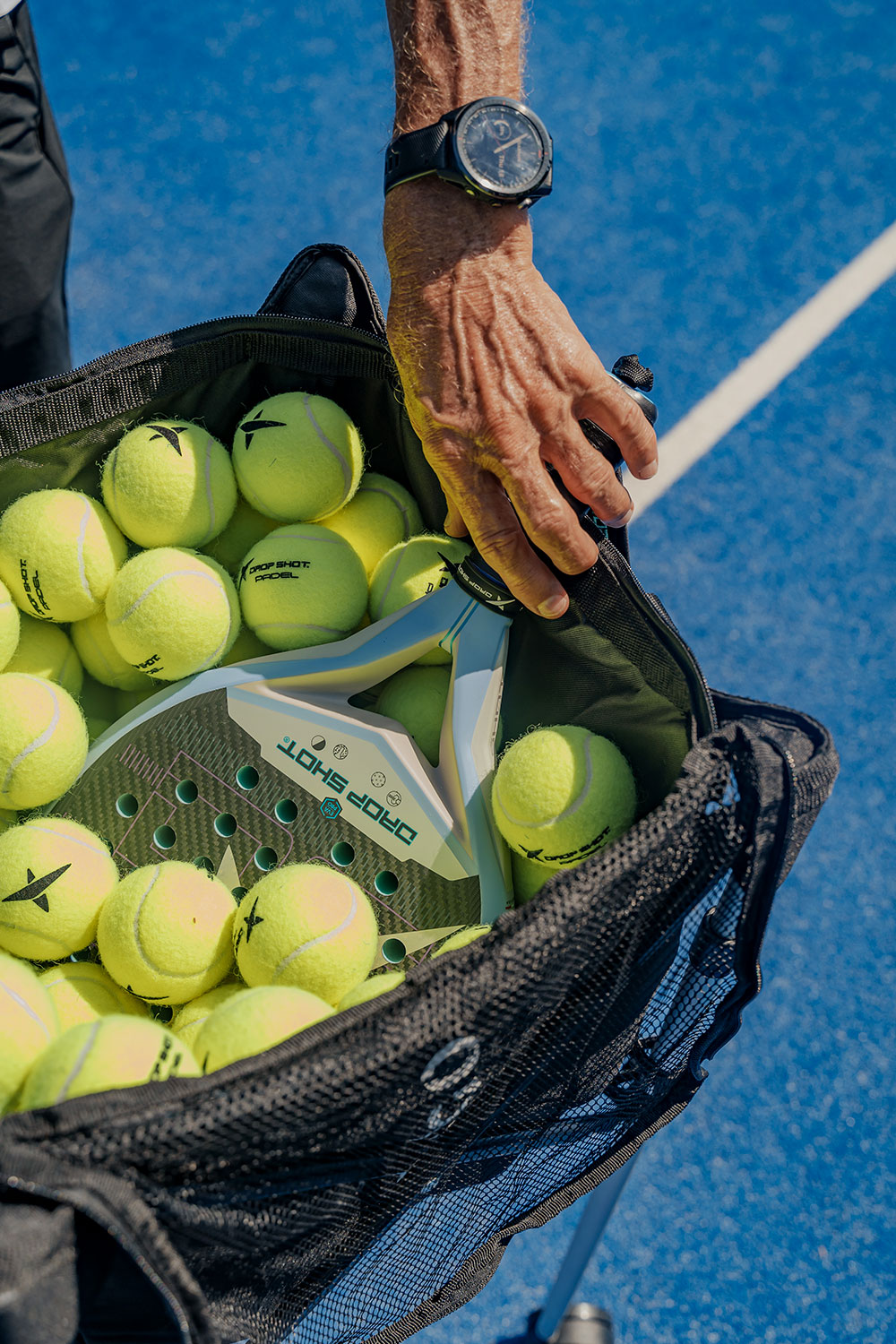 Close-up of a padel racket and bright yellow padel balls in a training bag at NIHI Sumba’s outdoor court.