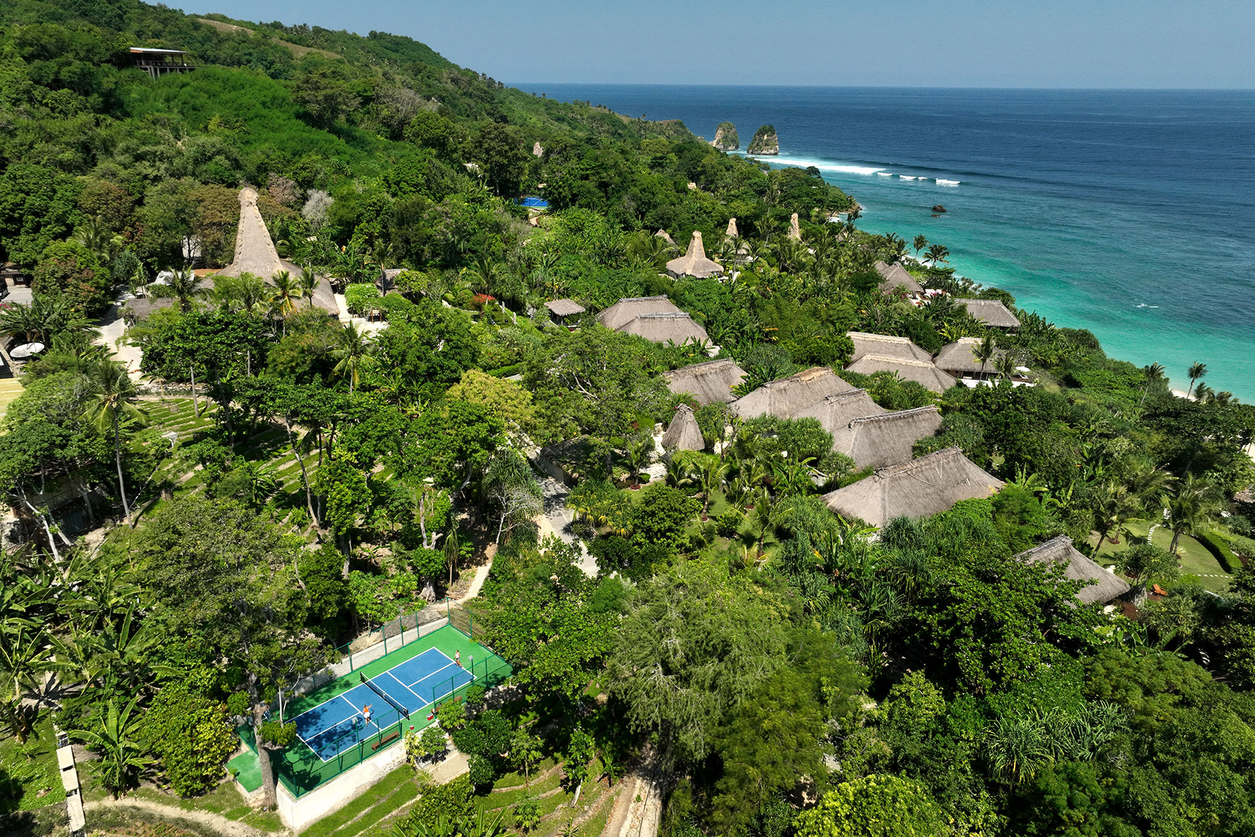A stunning aerial view of NIHI Sumba’s Pickleball Court nestled within lush greenery, with panoramic ocean views.