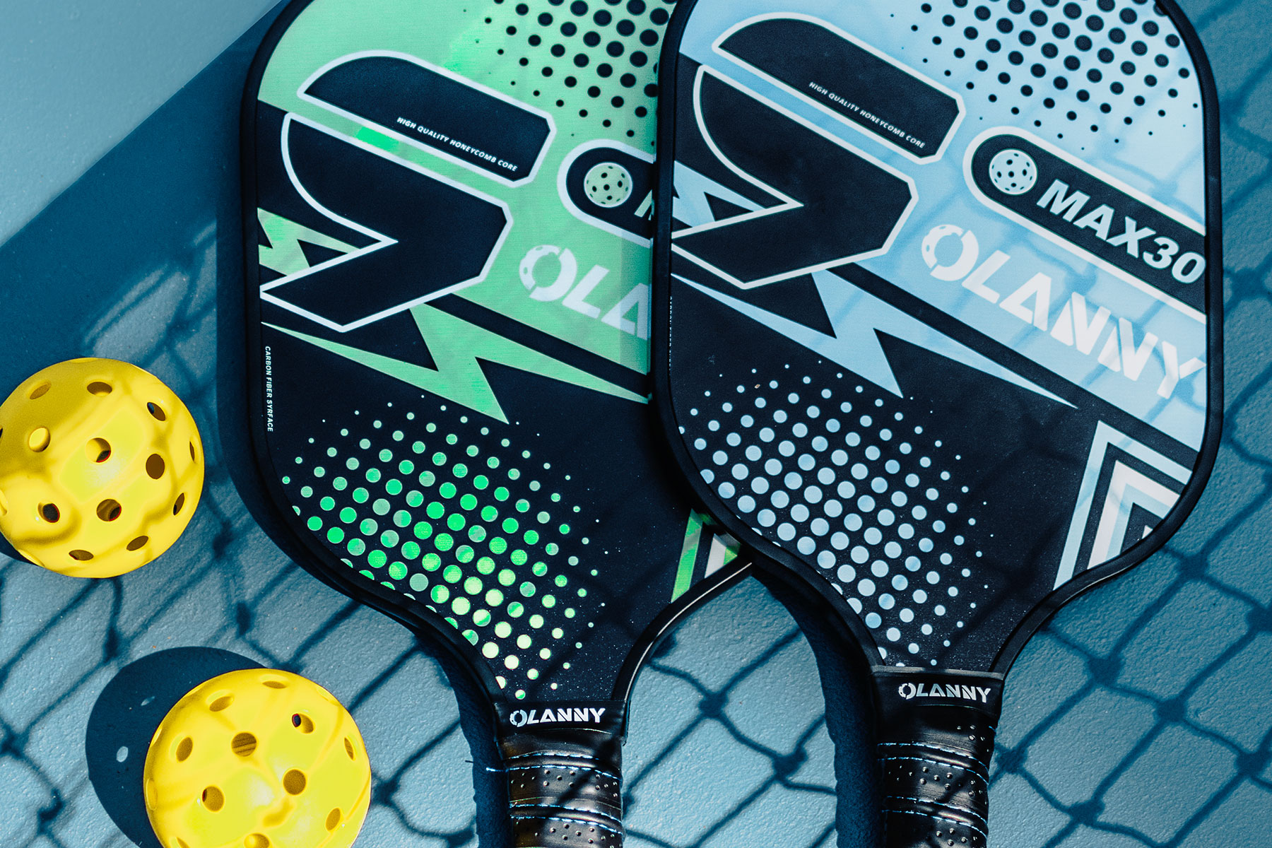 Close-up of two Pickleball paddles, one green and one blue, with yellow balls beside them, resting on a Pickleball court surface—ready for an exciting game at NIHI Sumba, where guests can enjoy this fun, sociable sport in a lush tropical setting.