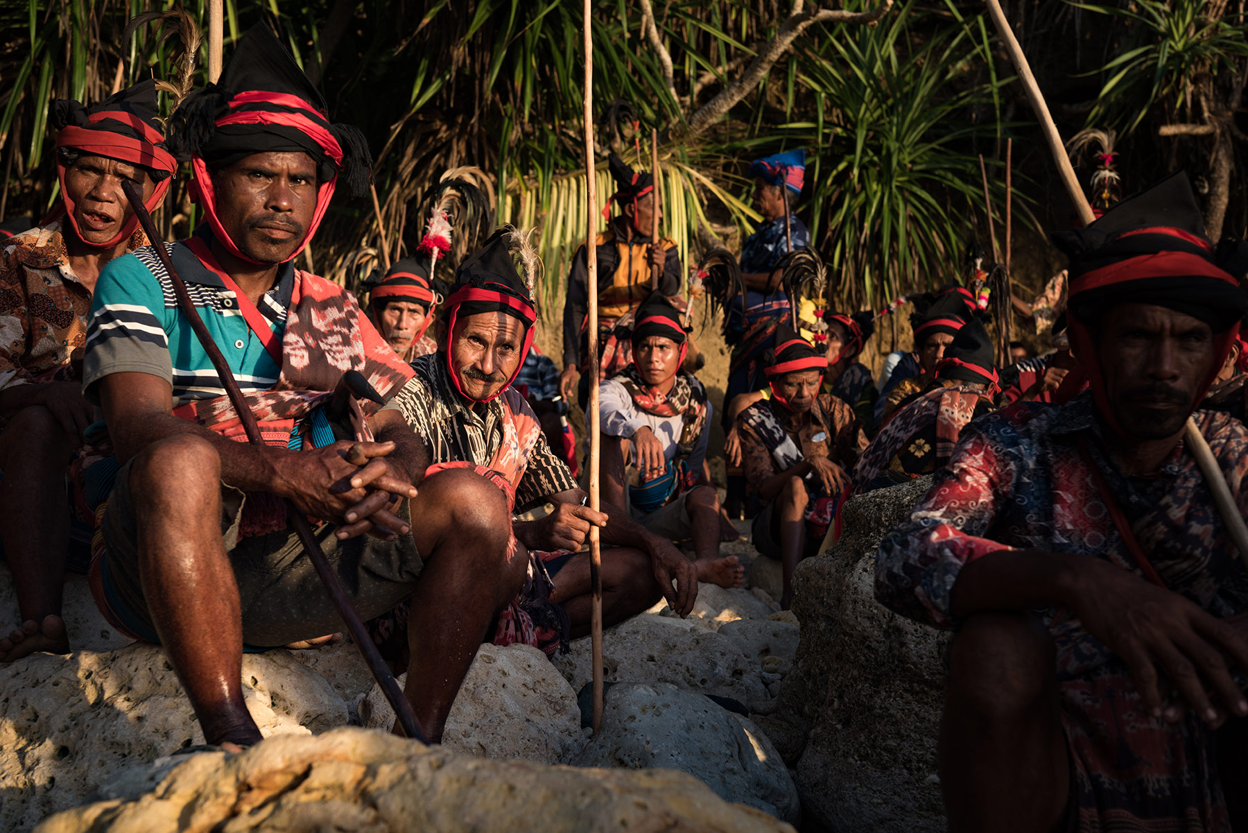 Sumbanese dressed in traditional attire with red and black headbands, seated with spears as they wait for the right moment to begin the sacred ceremony during Pasola Wanokaka, in Sumba, Indonesia.