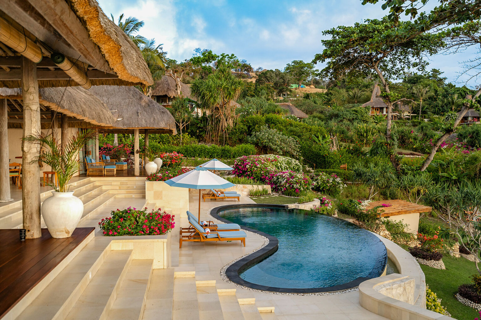 Scenic view of Putri Kasambi’s private pool area at NIHI Sumba, framed by tropical greenery, flowering plants, and thatched-roof villas near Occy’s Left.