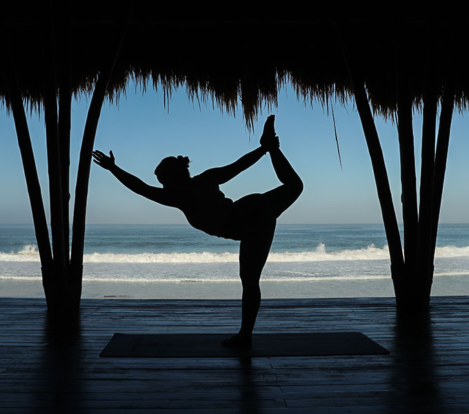 A yoga practitioner performing a graceful pose in the open-air yoga pavilion at NIHI Sumba, with a stunning view of Nihiwatu Beach and the Indian Ocean in the background, creating a serene and peaceful atmosphere.