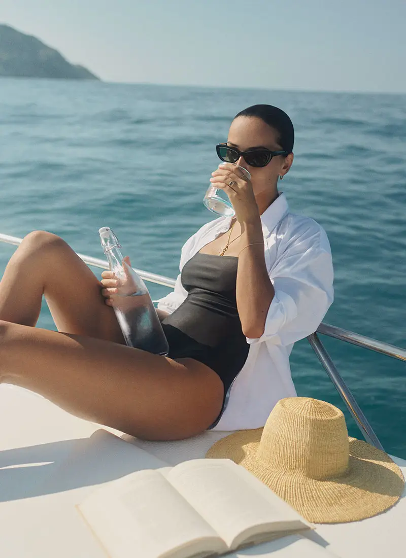 Woman relaxing on a luxury yacht with panoramic ocean views, anchored off the coast of Sumba Island, with the island’s rugged shoreline visible in the background during one of NIHI’s signature boat excursions.