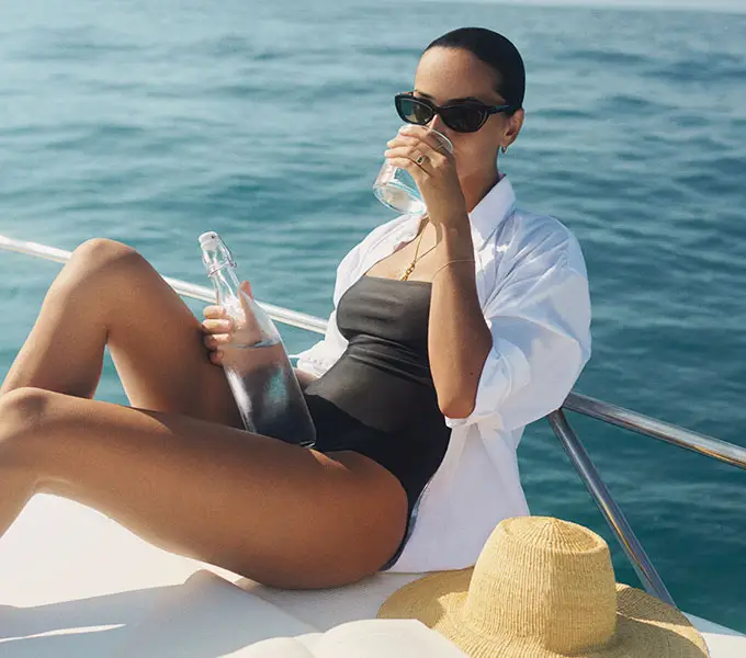 Woman relaxing on a luxury yacht with panoramic ocean views, anchored off the coast of Sumba Island, with the island’s rugged shoreline visible in the background during one of NIHI’s signature boat excursions.