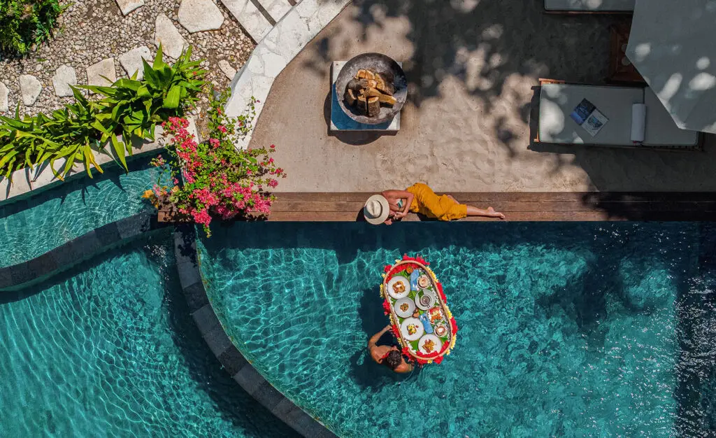 Overhead view of a floating breakfast setup in a private pool at NIHI Sumba, with a couple enjoying the experience surrounded by tropical greenery.