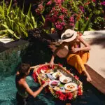 Couple enjoying a tropical floating breakfast in a private pool surrounded by vibrant flowers and lush greenery at NIHI Sumba.