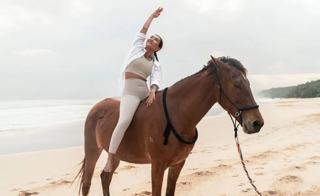 Woman practicing mindful stretching atop a calm Sumba horse on Nihiwatu Beach at NIHI Sumba, during a Horse Yoga session designed to deepen body awareness and emotional balance in a serene coastal setting.