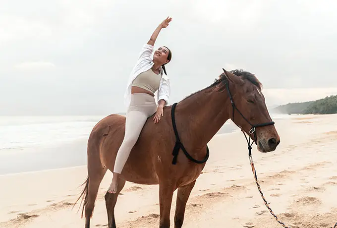 Woman practicing mindful stretching atop a calm Sumba horse on Nihiwatu Beach at NIHI Sumba, during a Horse Yoga session designed to deepen body awareness and emotional balance in a serene coastal setting.