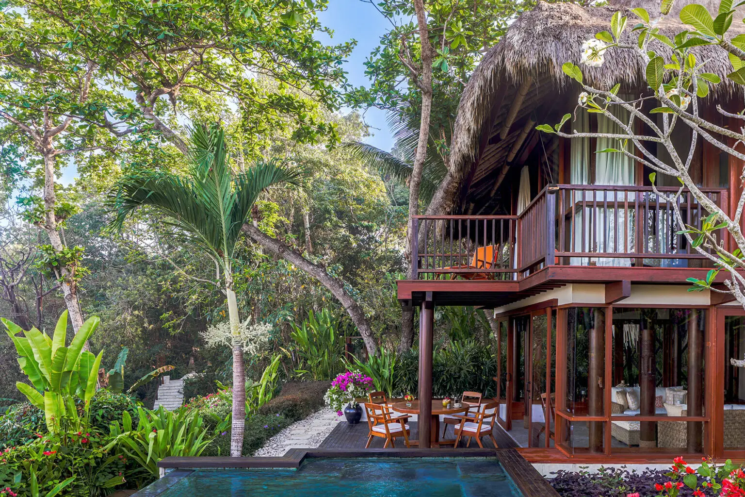 The Kanatar Villa at NIHI® Sumba, showcasing a private dining area next to the plunge pool, with a balcony offering a view of lush greenery and a tropical garden.