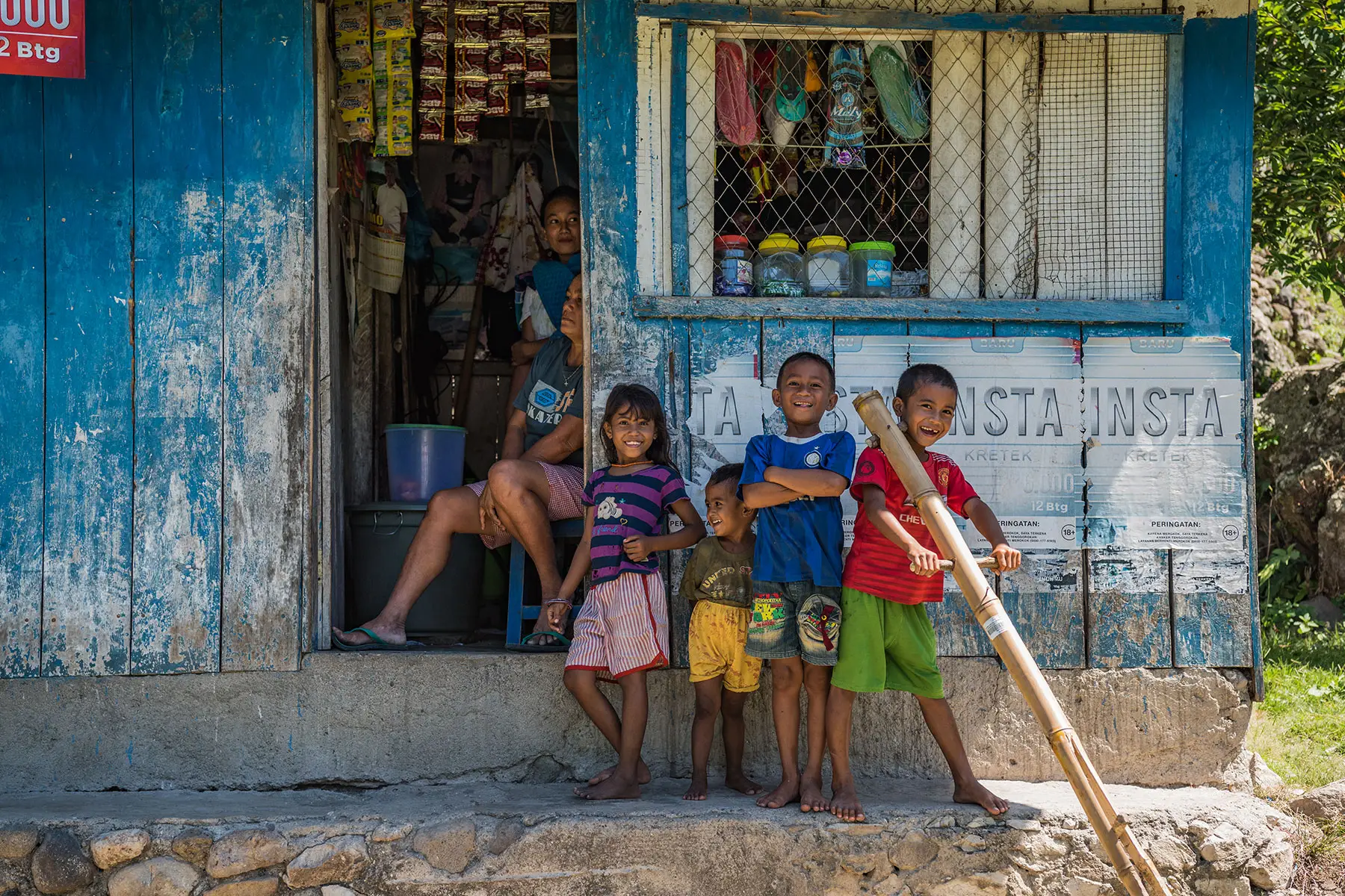 Smiling Sumbanese children standing outside a rustic village shop, showcasing the warmth and charm of local life in rural Sumba.