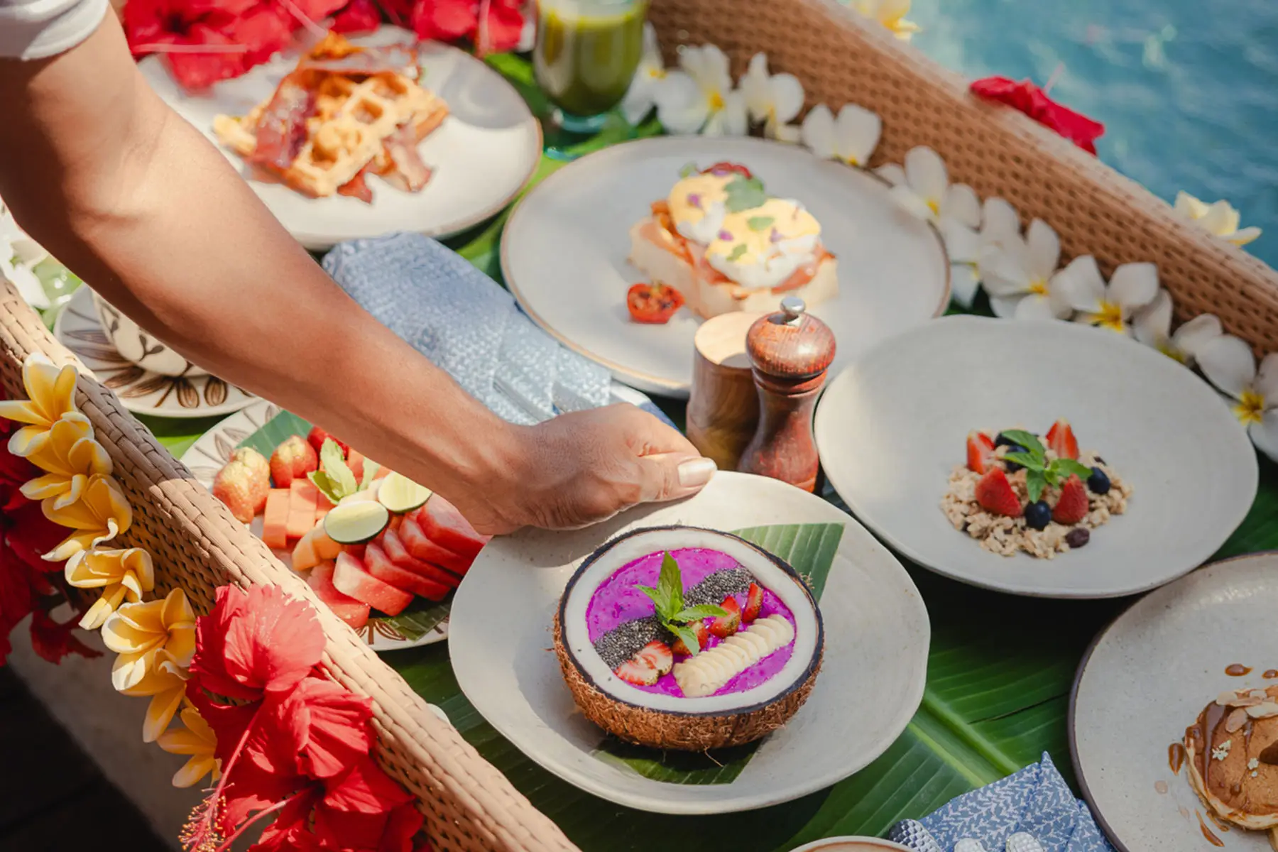 Tropical floating breakfast tray at NIHI Sumba, adorned with fresh flowers and featuring a coconut smoothie bowl, fresh fruit, granola, and gourmet dishes.