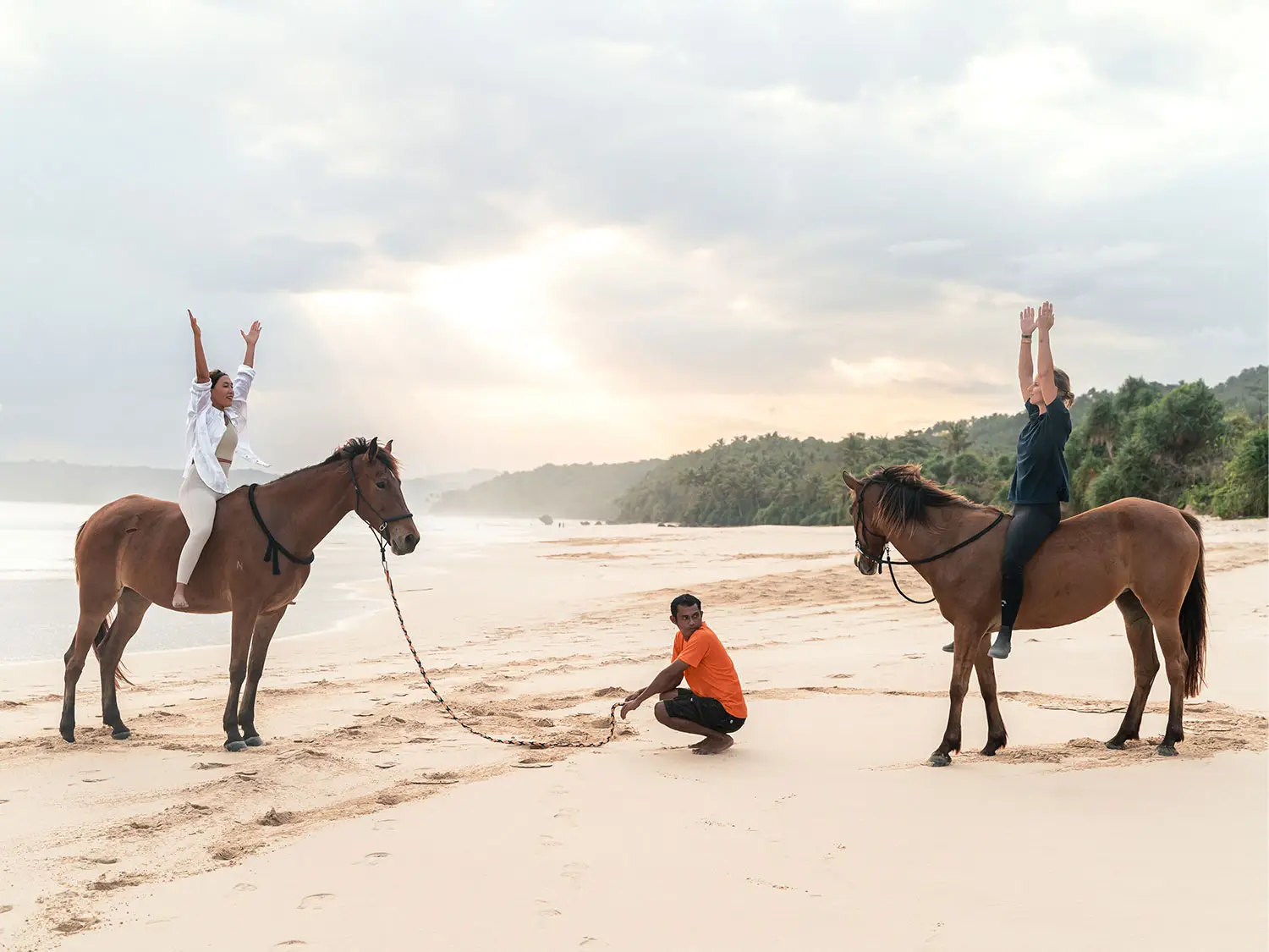Guests practice yoga stretches while seated on horseback during a sunrise Horse Yoga session at NIHI Sumba’s beach, guided by an equestrian team member, creating a serene connection with nature and Sumba’s spirited horses.