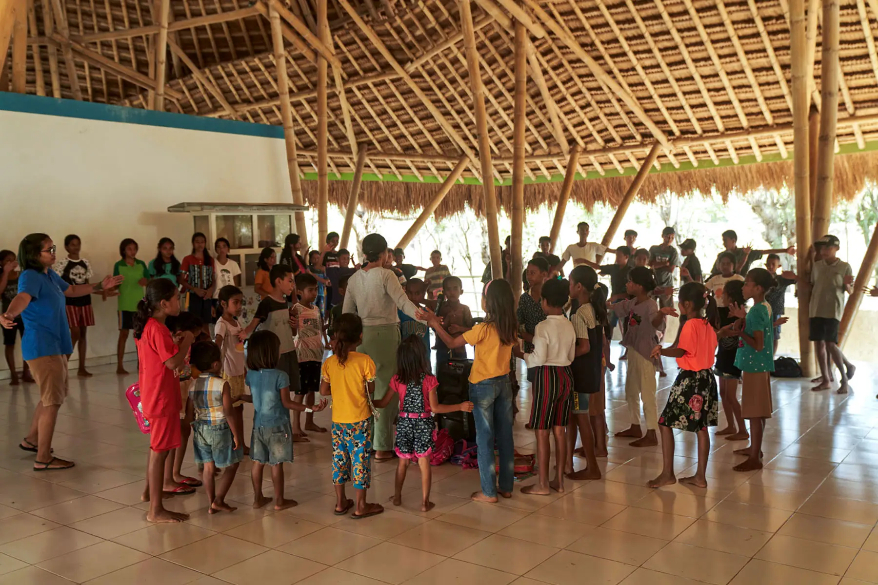 Sumbanese children joyfully participating in an English class activity at the Learning Development Center, supported by NIHI Sumba and the Burch Family Foundation, to enhance language and social skills through songs and interactive learning.