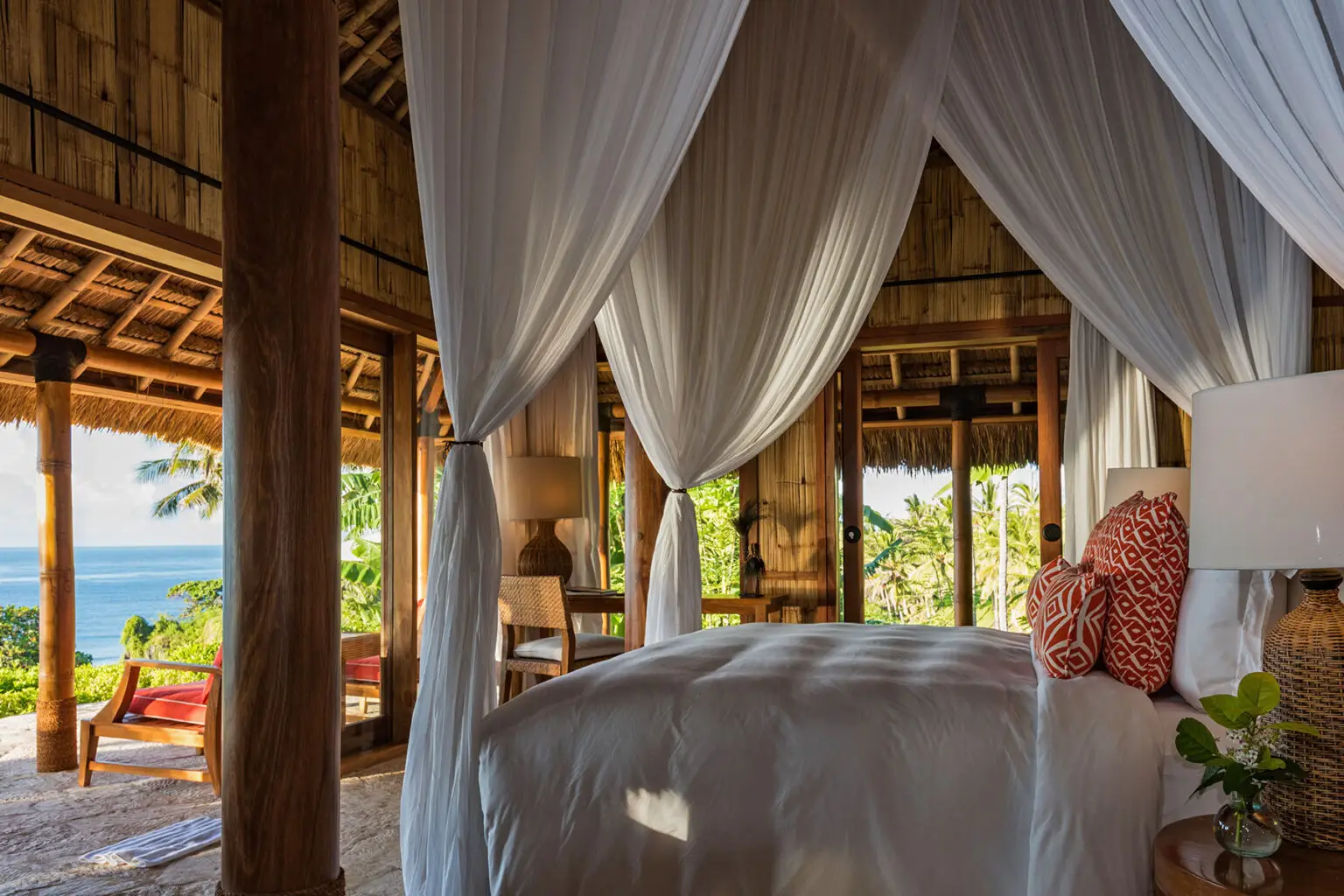 Canopy-draped bed in Villa Rahasia, the only private villa within the grounds of NIHI Sumba’s Nihioka Spa, offering panoramic ocean views, rustic bamboo interiors, and floor-to-ceiling glass doors that blend indoor comfort with surrounding nature. Guests can book it for the first or last night of their stay at the resort.