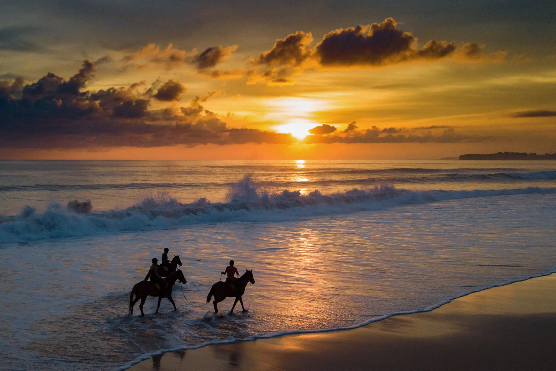 Two riders on Sumba horses are silhouetted against a glowing sunset at Nihiwatu Beach during NIHI Sumba’s Sunset Beach Horse Riding experience.