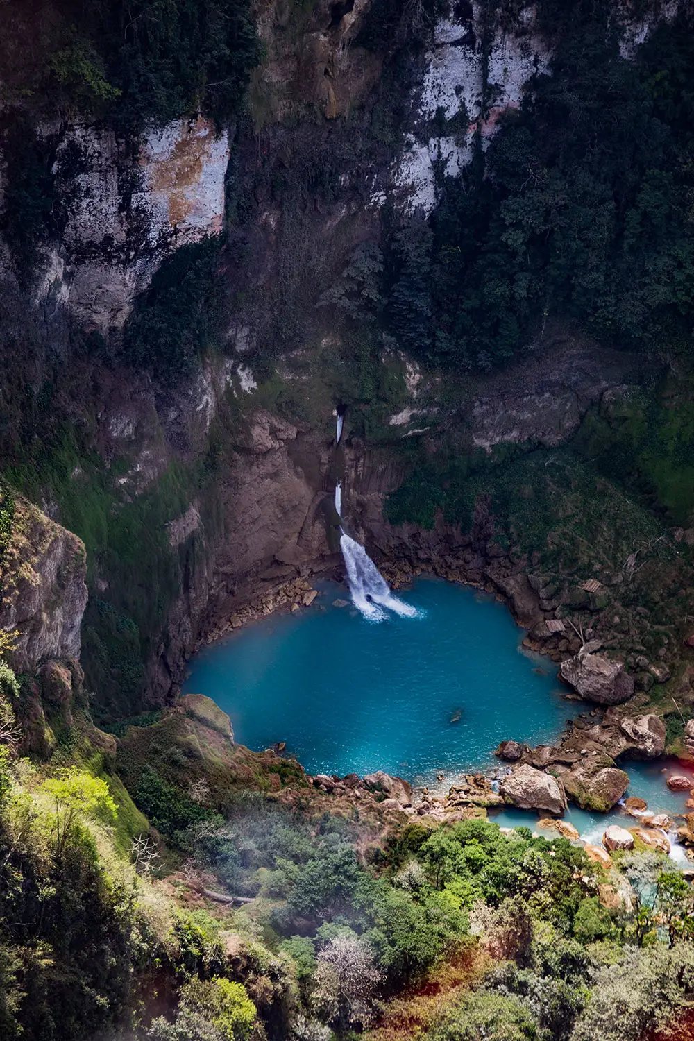 Aerial view of the remote Blue Waterfall, featuring a vivid turquoise plunge pool and natural stone basins surrounded by cliffs and dense jungle.