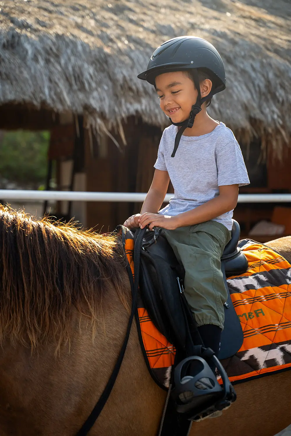 Smiling child riding a Sumba pony at NIHI Sumba’s Kids Pony Club, learning horsemanship at Sandalwood Stables.
