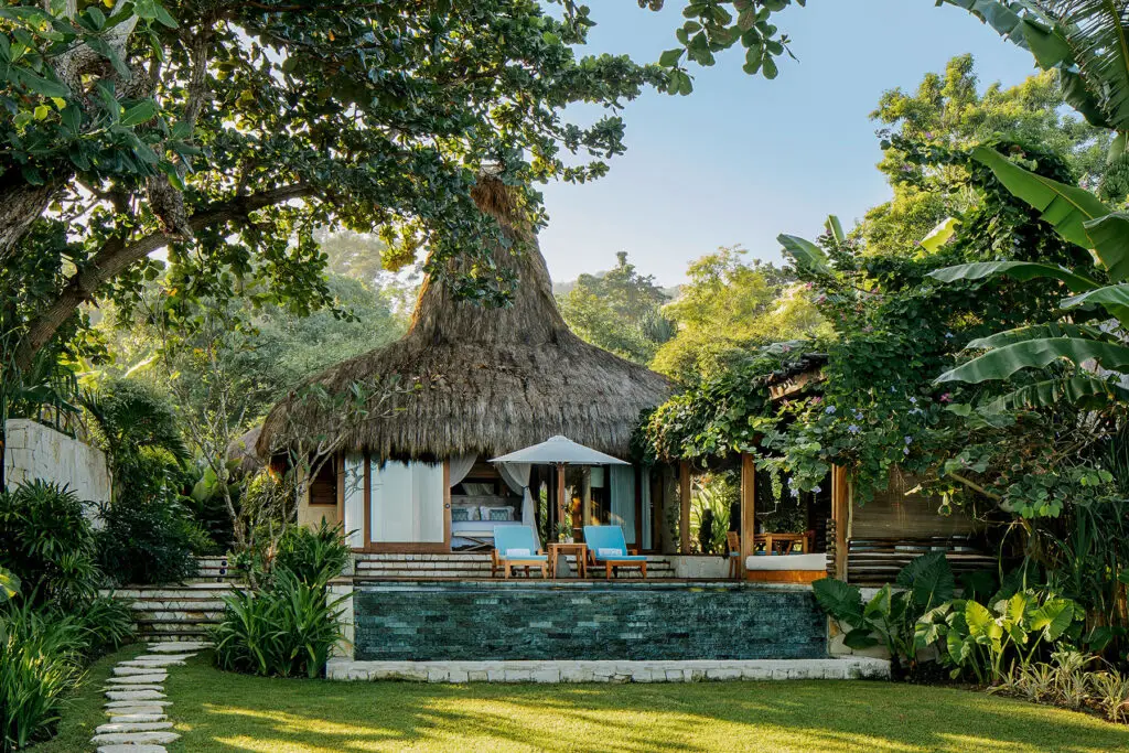 View of the Marangga Villa at NIHI Sumba, featuring a thatched roof, outdoor lounge area, and lush tropical surroundings, showcasing the villa's serene and natural beauty.