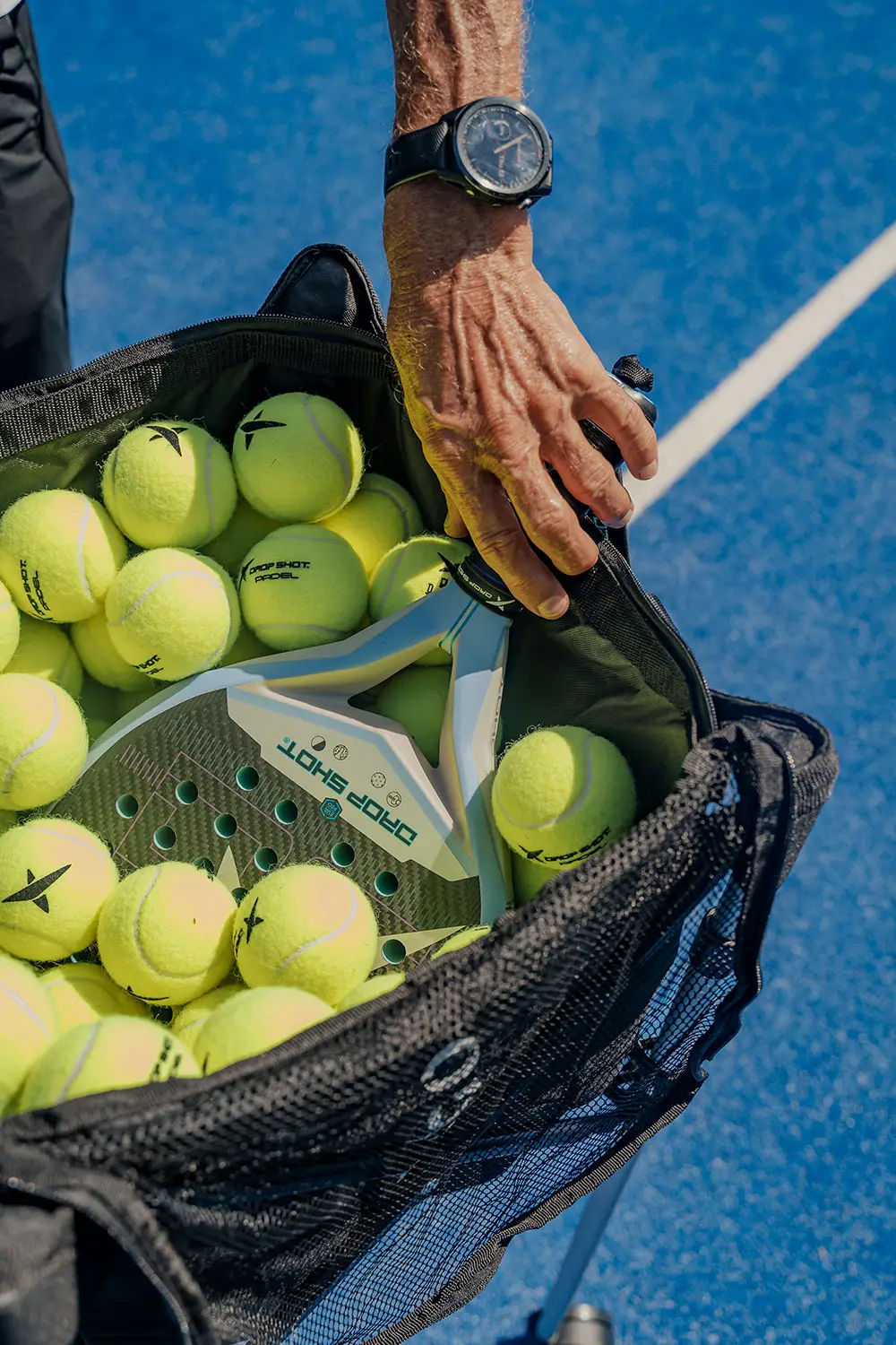 Close-up of a padel racket and bright yellow padel balls in a training bag at NIHI Sumba’s outdoor court.