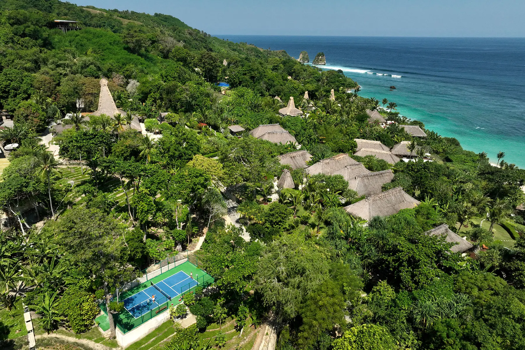 A stunning aerial view of NIHI Sumba’s Pickleball Court nestled within lush greenery, with panoramic ocean views.