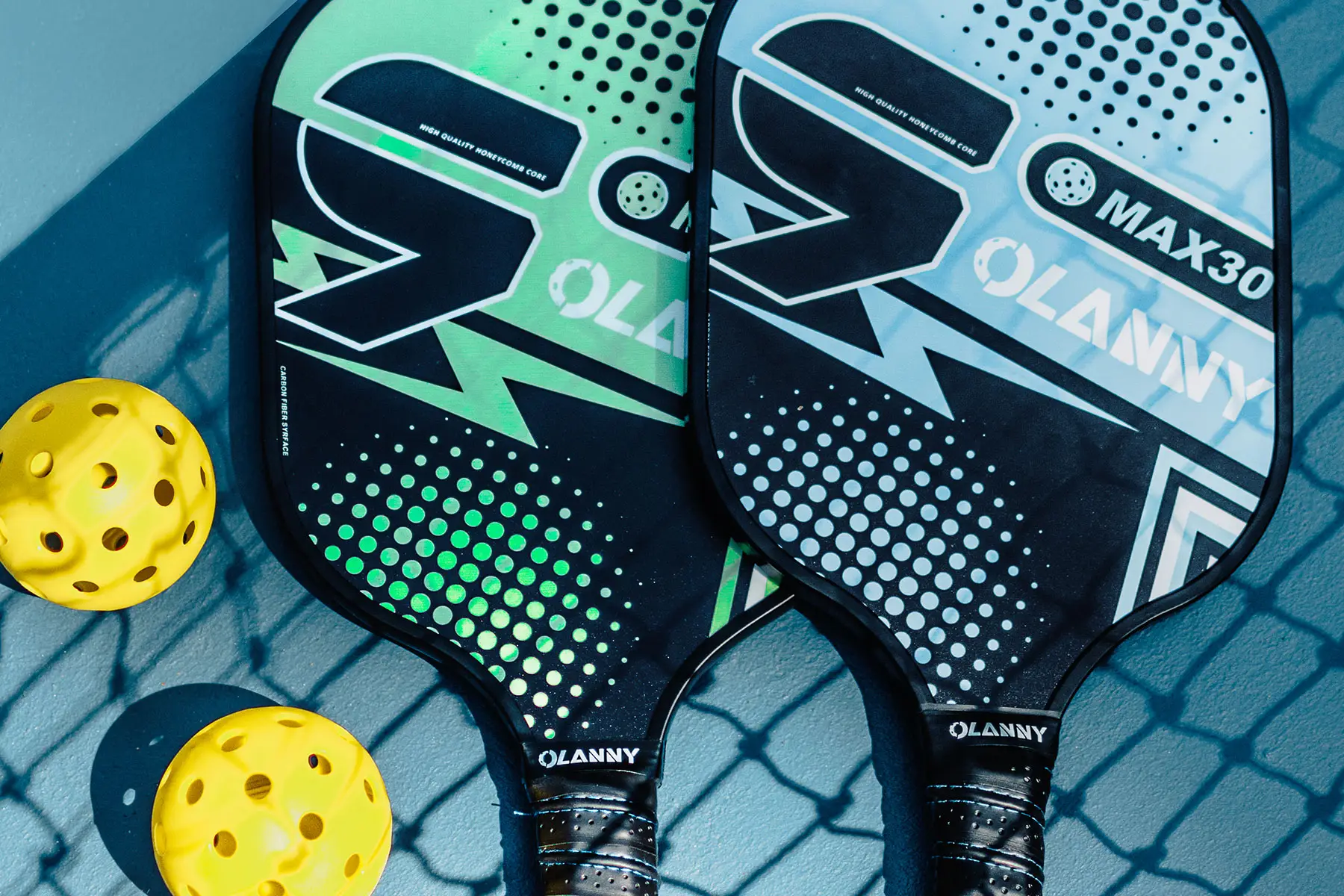 Close-up of two Pickleball paddles, one green and one blue, with yellow balls beside them, resting on a Pickleball court surface—ready for an exciting game at NIHI Sumba, where guests can enjoy this fun, sociable sport in a lush tropical setting.