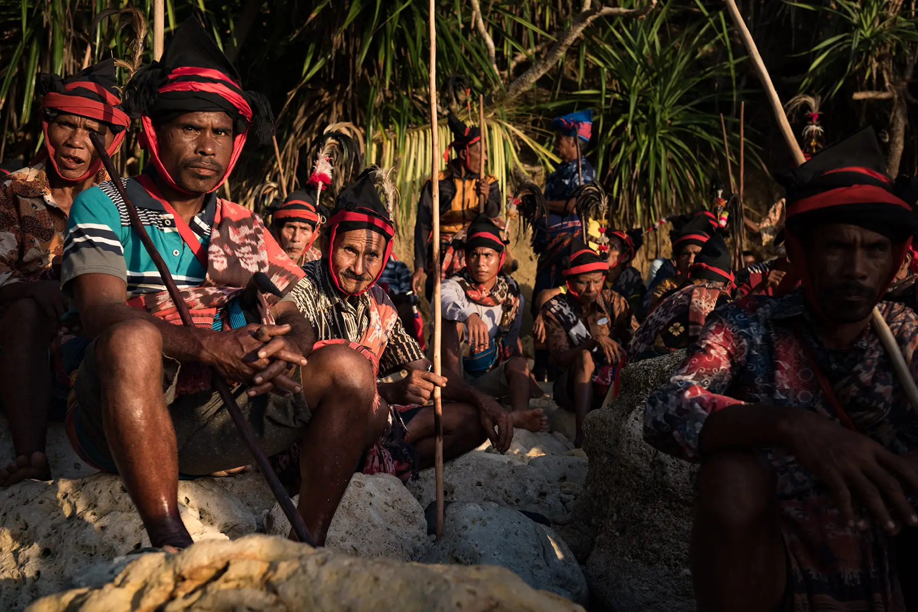 Sumbanese dressed in traditional attire with red and black headbands, seated with spears as they wait for the right moment to begin the sacred ceremony during Pasola Wanokaka, in Sumba, Indonesia.