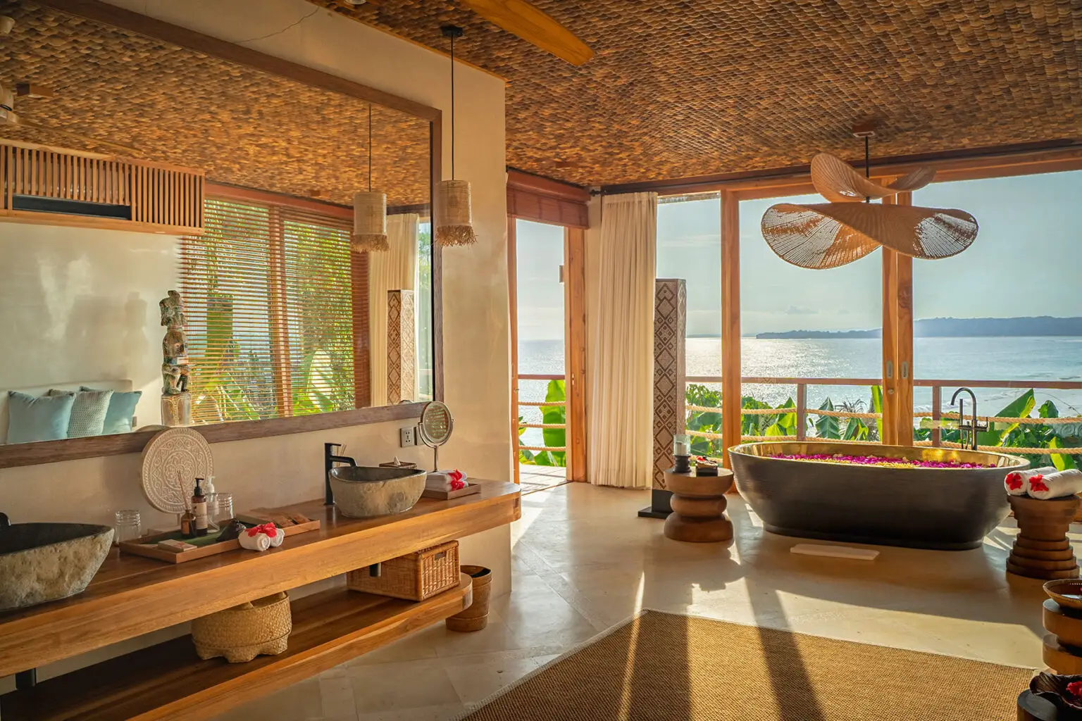 Elegant ocean-view bathroom at Putri Kasambi featuring a flower-filled soaking tub, woven ceiling, and warm natural light at NIHI Sumba.
