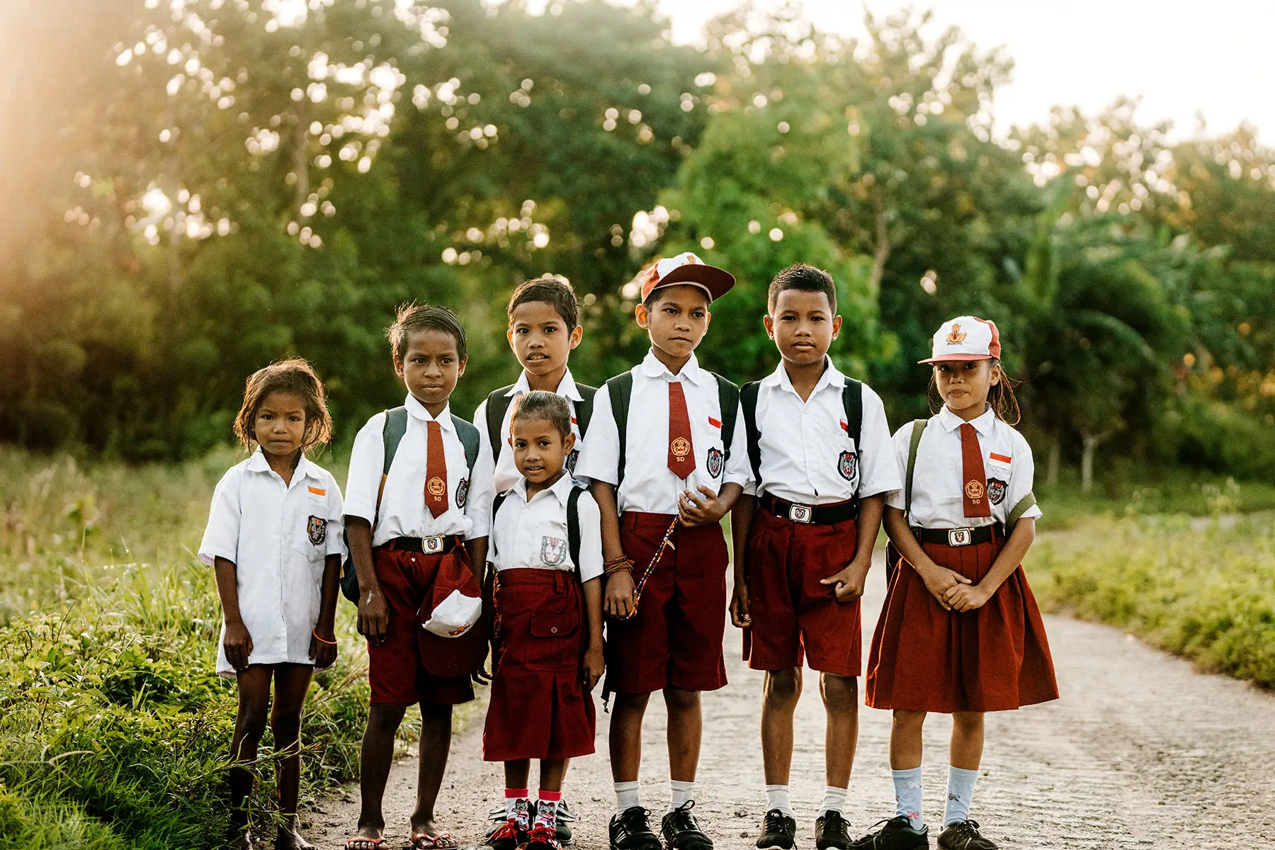 Group of young Sumbanese schoolchildren dressed in crisp white shirts and red uniforms, standing barefoot and in sandals on a rural path at sunrise, symbolizing the Sumba Foundation’s impact on education access in remote communities.