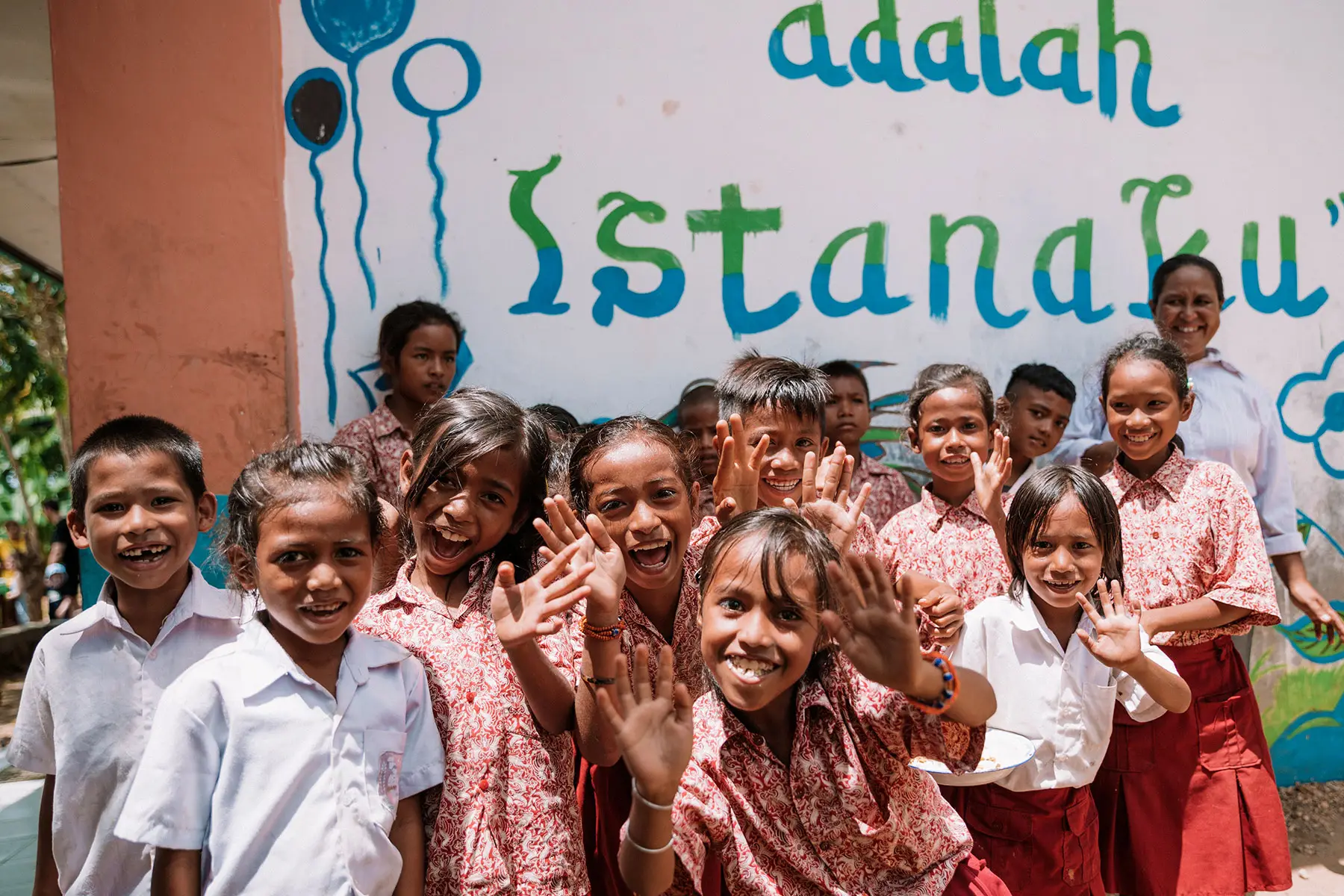 Joyful group of Sumbanese school children smiling and waving outside their classroom, capturing the vibrant spirit and educational impact of initiatives by the Sumba Foundation and Burch Family Foundation