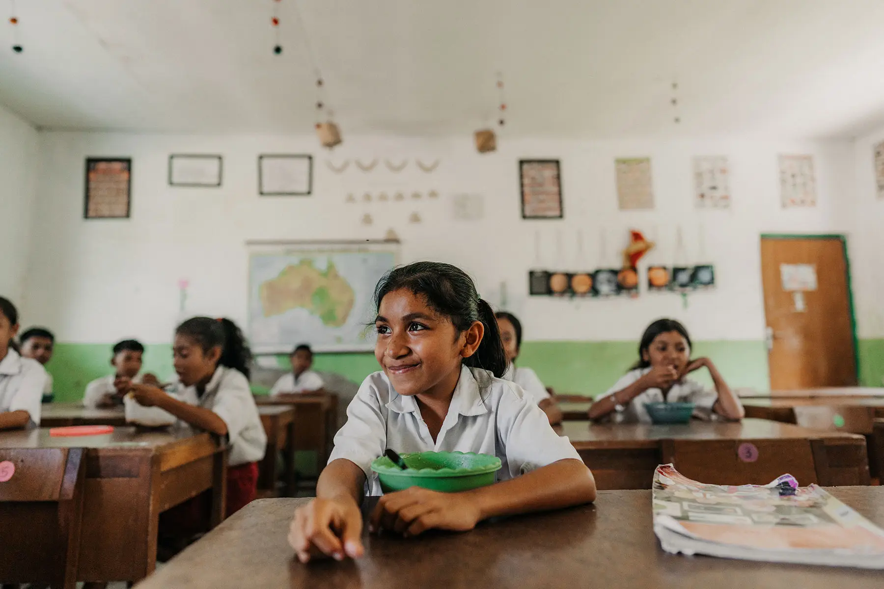 A smiling schoolgirl in uniform enjoys her meal inside a classroom in Sumba, reflecting the educational and nutritional impact of the Sumba Foundation’s outreach programs.