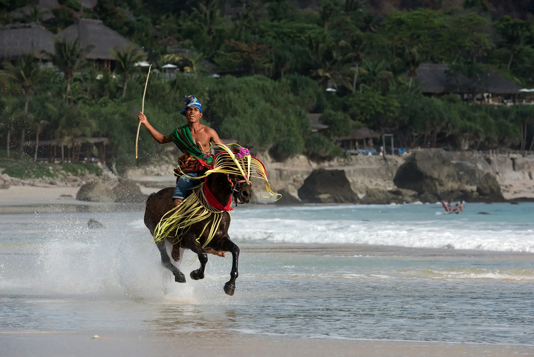 Sumbanese horseman galloping along the beach in traditional attire during Pasola demonstration at NIHI Sumba, Indonesia.