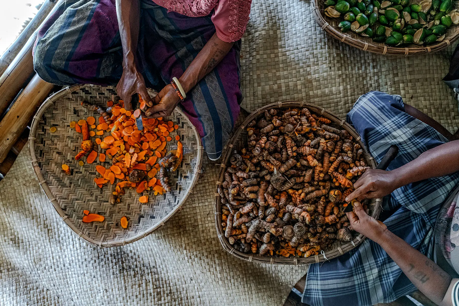 Women in traditional attire preparing freshly harvested turmeric for the Sumba 7 Botanical Elixir using ancestral slicing techniques on woven mats.