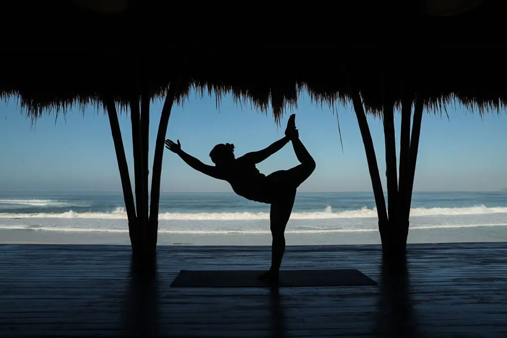 A yoga practitioner performing a graceful pose in the open-air yoga pavilion at NIHI Sumba, with a stunning view of Nihiwatu Beach and the Indian Ocean in the background, creating a serene and peaceful atmosphere.