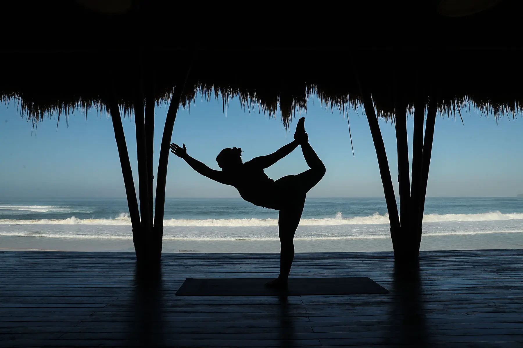 A yoga practitioner performing a graceful pose in the open-air yoga pavilion at NIHI Sumba, with a stunning view of Nihiwatu Beach and the Indian Ocean in the background, creating a serene and peaceful atmosphere.
