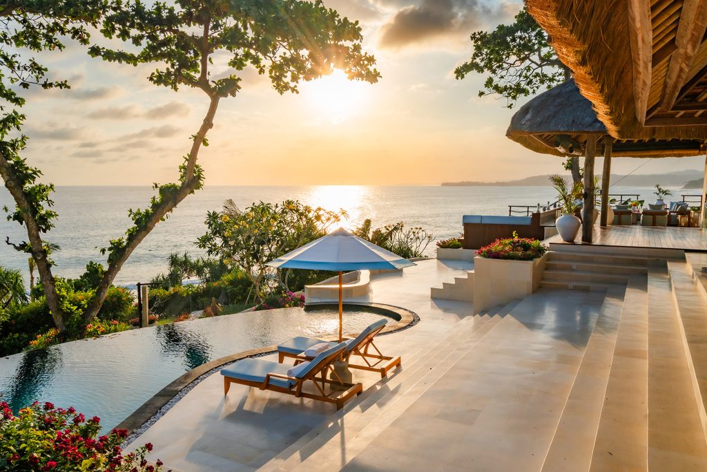Oceanfront infinity pool and sun loungers at Putri Kasambi Villa, overlooking a golden sunset and Occy’s Left surf break at NIHI Sumba — surrounded by lush tropical landscaping and ideal for surf-loving travelers seeking barefoot luxury.